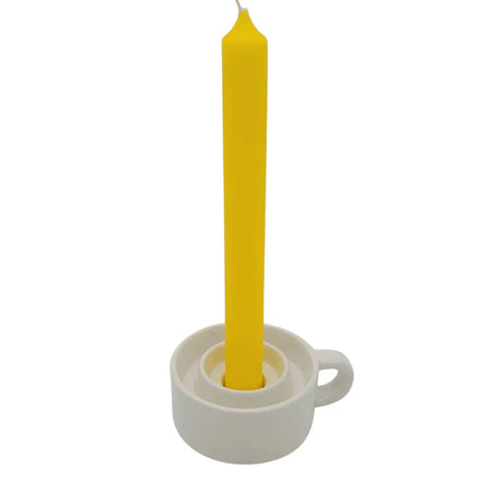 A vibrant yellow taper candle in a minimalist white ceramic tealight and dinner candle holder