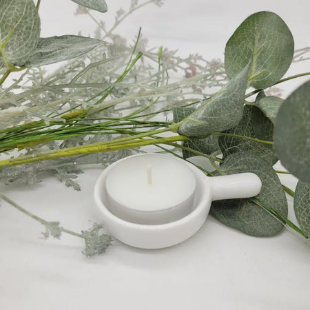 White ceramic tealight candle holder with small handle shaped like a spoon for holding tealight candles