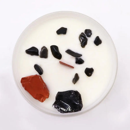 White candle with black and red stone fragments in wax for root chakra balance chakra crystal candle