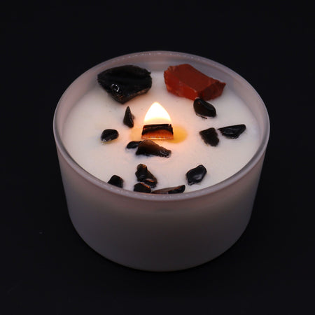 A white frosted glass root chakra candle with a lit flame and black and red stone chips on top