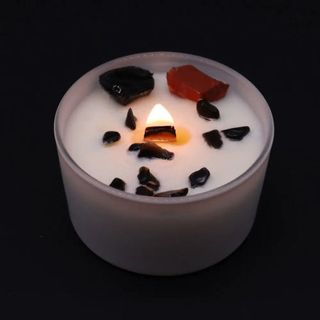A white frosted glass root chakra candle with a lit flame and black and red stone chips on top