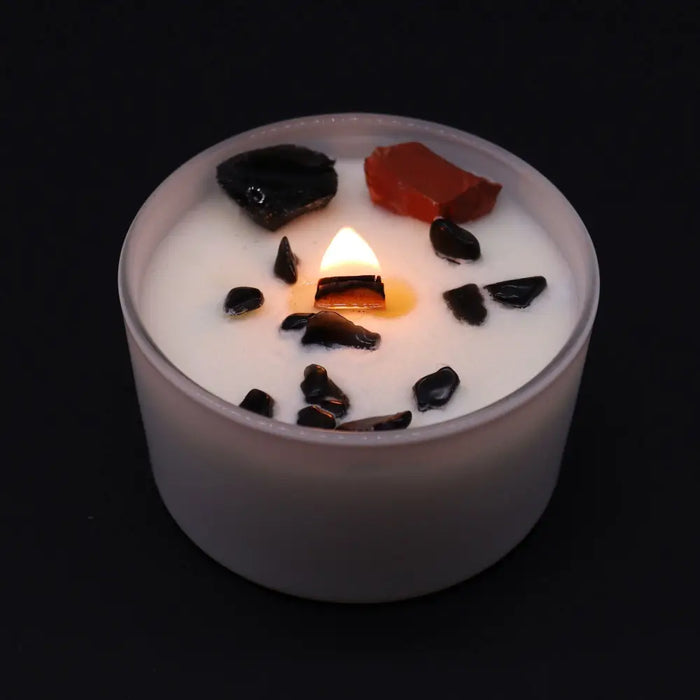 A white frosted glass root chakra candle with a lit flame and black and red stone chips on top