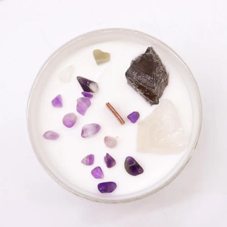 A white candle in a glass jar with amethyst, obsidian, and quartz stones for crown chakra spiritual connection