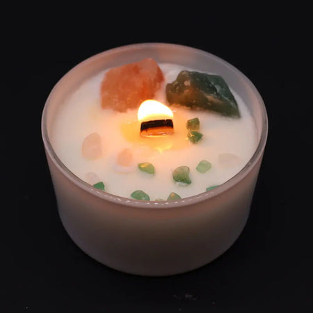 A white chakra crystal candle in a frosted jar with a lit wooden wick pink himalayan salt and green stones