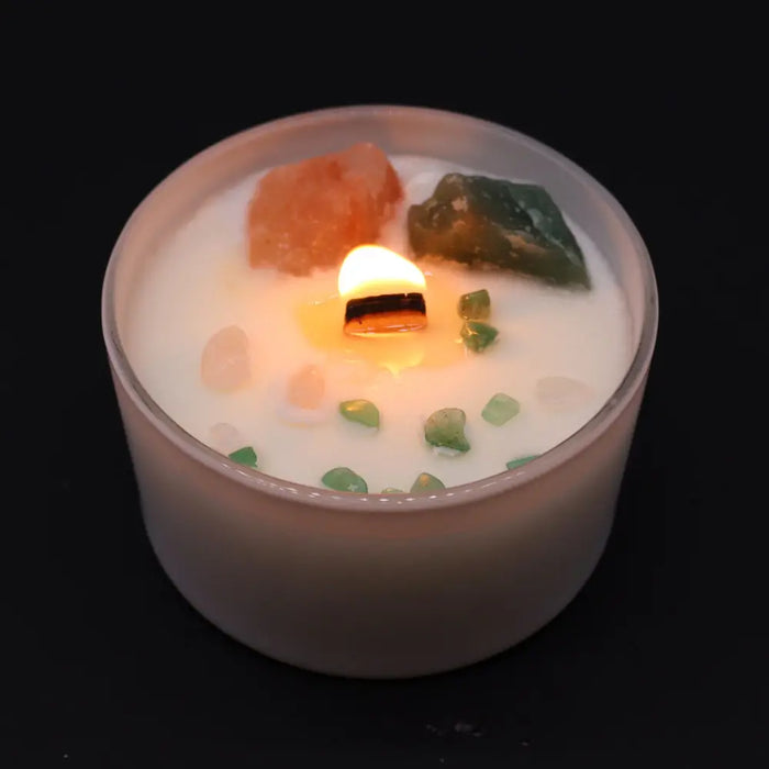A white chakra crystal candle in a frosted jar with a lit wooden wick pink himalayan salt and green stones