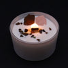 A white sacral chakra candle with a lit wooden wick and scattered dark and pinkish crystal fragments on top