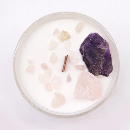 A white candle in a glass jar with pink and purple crystals including amethyst for third eye chakra healing