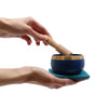 Deep blue tibetan chakra singing bowl with gold rim held in hands and struck by wooden mallet in bowl gift set