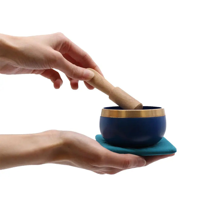 Deep blue tibetan chakra singing bowl with gold rim held in hands and struck by wooden mallet in bowl gift set