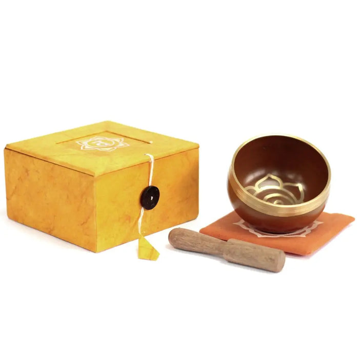 Bronze chakra singing bowl with gold rim and lotus engraving resting on orange cloth next to wooden mallet for sacral chakra