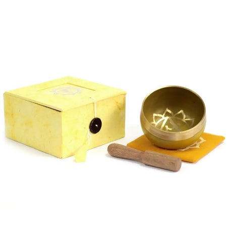 Golden chakra singing bowl with lotus design for solar plexus chakra on orange cloth next to yellow box and wooden mallet