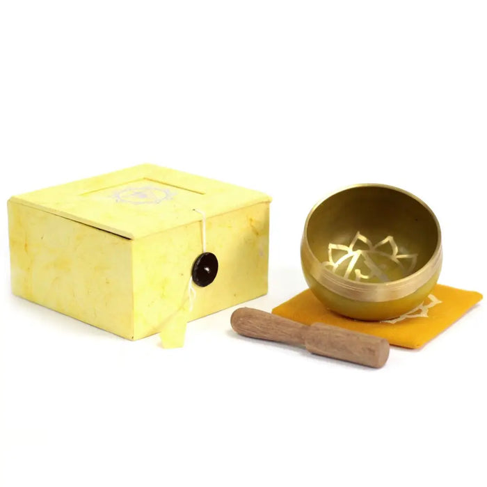 Golden chakra singing bowl with lotus design for solar plexus chakra on orange cloth next to yellow box and wooden mallet