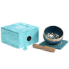 Deep blue chakra singing bowl with gold rim and throat chakra design next to a wooden mallet for chakra singing