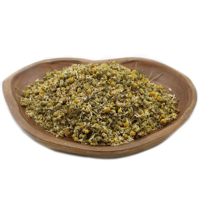 A heart-shaped wooden bowl filled with dried yellow chamomile heads for herbal use and tea