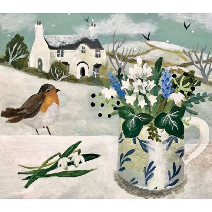 A white ceramic mug with blue leaf pattern holds white and blue flowers alongside christmas cards by sarah bowman featuring snowy owl