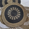 Handwoven circular seagrass rug in natural and black tones with a radial pattern and braided edges