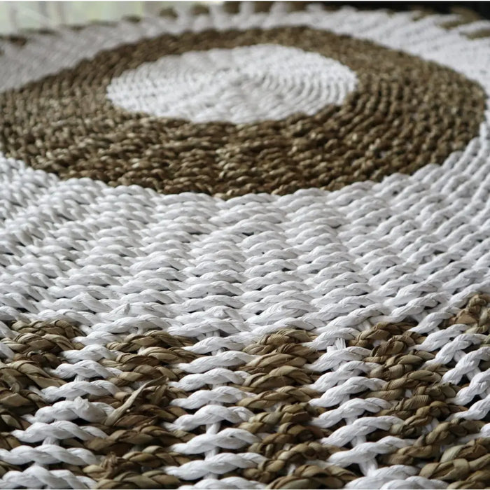 A handcrafted circular seagrass rug with woven texture in white and natural brown arranged in concentric rings