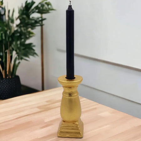A sleek black candle in a glossy gold ceramic candle holder with a classic fluted design stands upright