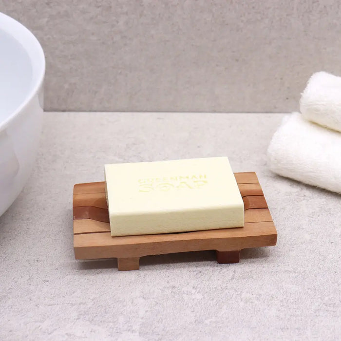 A pale yellow soap bar resting on a classic naseberry wood soap dish with slatted grid drainer design