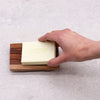 A pale yellow greenman soap bar resting on a classic naseberry wood soap dish with a slatted grid drainer design