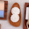 Two white flower-shaped bath bombs in a smooth light brown classic naseberry wood soap dish with organic shape