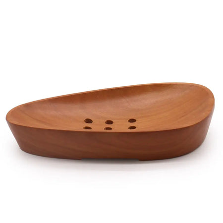 A smooth medium-brown naseberry wood soap dish with a curved boat shape and six drainage holes