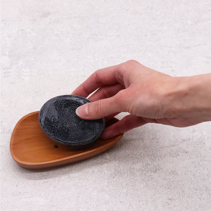 Dark gray speckled soap resting in a light brown classic naseberry wood soap dish with an organic shape