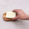A light beige soap with greenman soap embossed in gold resting on a naseberry wood oval soap dish