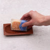 A rectangular soap with orange and blue swirls resting on a naseberry wood soap dish rectangle