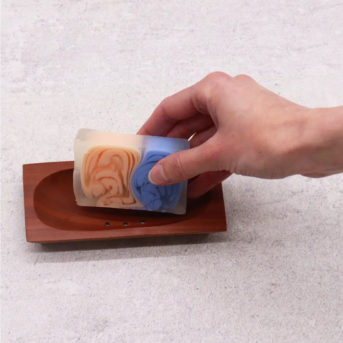 A rectangular soap with orange and blue swirls resting on a naseberry wood soap dish rectangle
