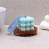A light blue bubbly cube soap with ribbon on a round brown naseberry wood soap dish