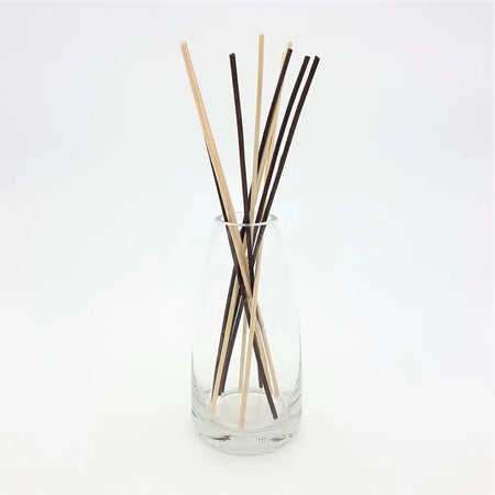 A clear glass reed diffuser vase holding natural wood and dark brown diffuser sticks