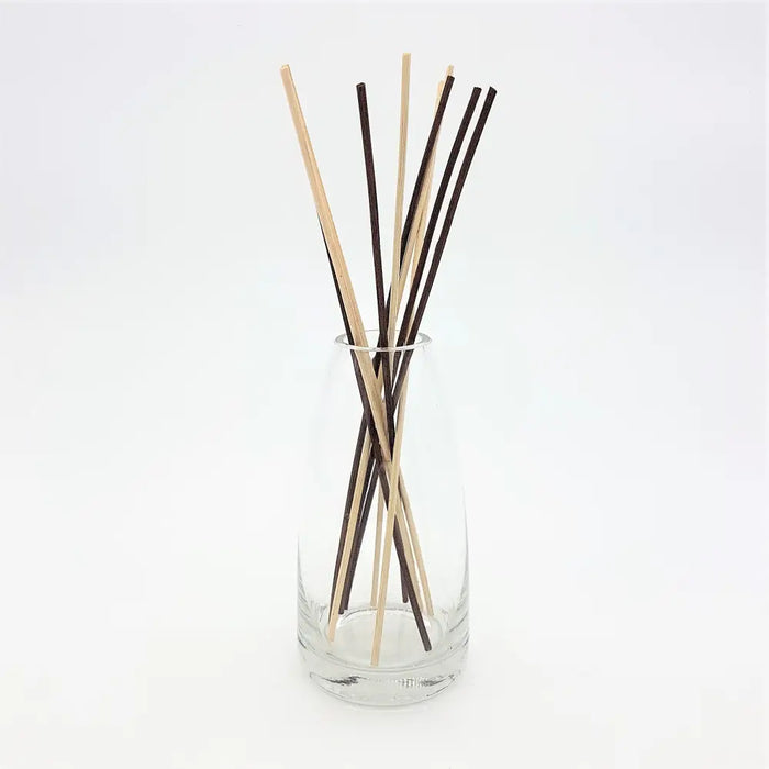 A clear glass reed diffuser vase holding natural wood and dark brown diffuser sticks