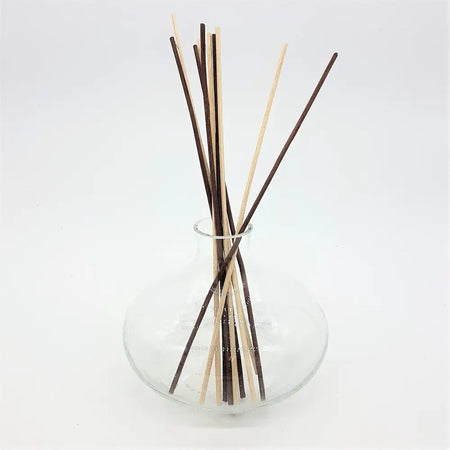 A clear glass reed diffuser bottle vase squat shaped holding natural wood and dark brown reeds