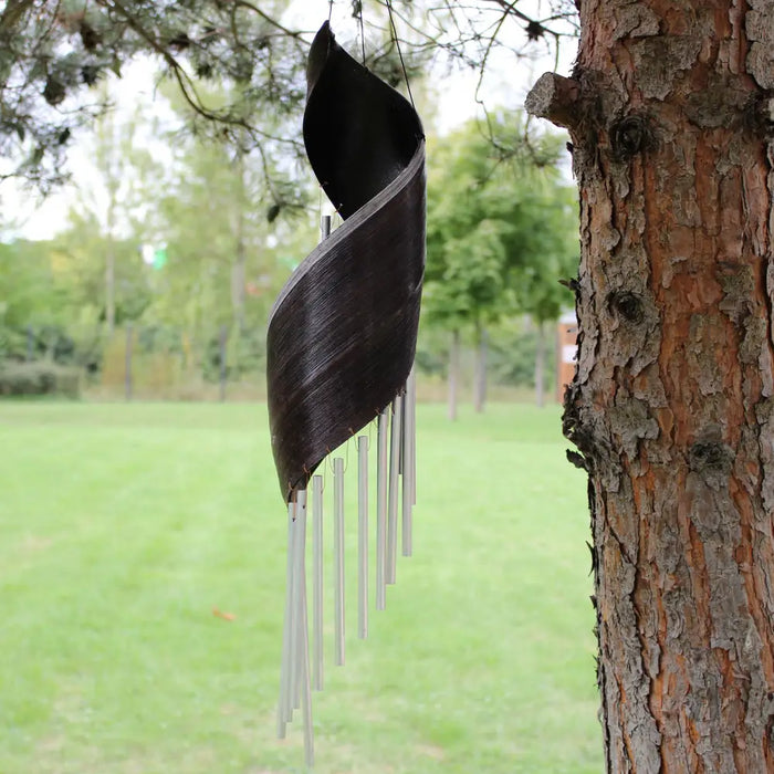 Black spiral metal wind chime with silver tubes hanging from a tree featuring coconut leaf design wind chimes chocolate