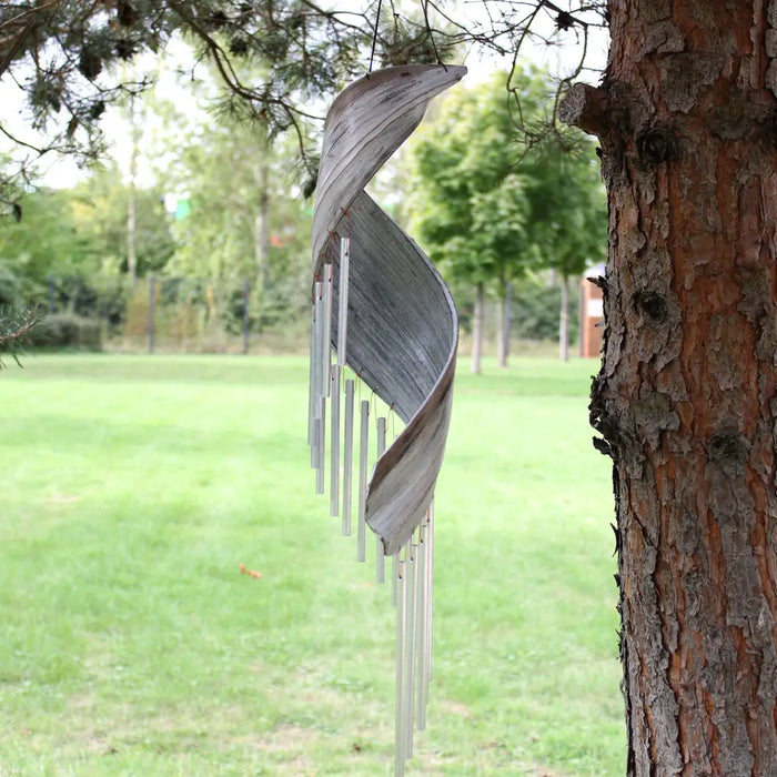 A weathered silver metal wind chime with spiral design and hanging rods in a whitewash coconut leaf style