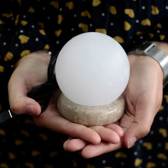 A smooth white usb crystal rock himalayan salt lamp with a textured beige stone base showing its hygroscopic properties