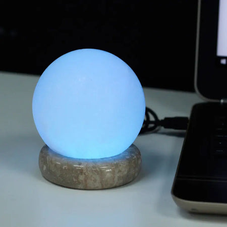 A glowing blue colour-changing usb crystal rock himalayan salt lamp ball with textured stone base showing hygroscopic properties