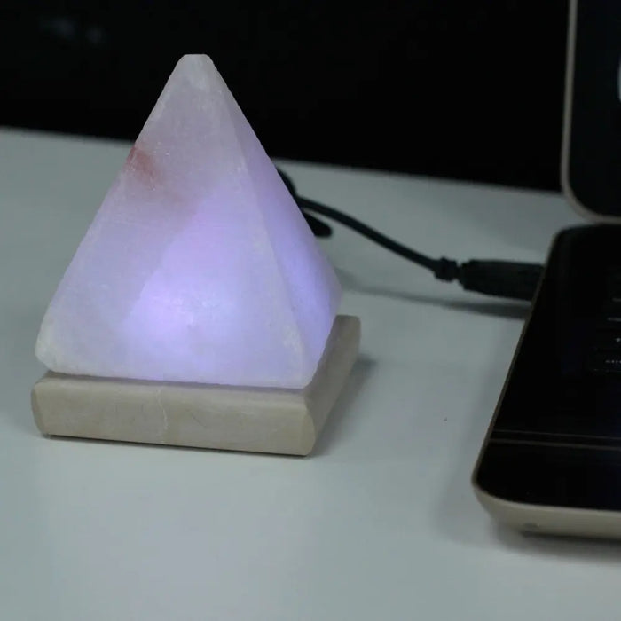 A glowing white himalayan salt lamp pyramid with usb crystal rock and a pinkish hue showing its hygroscopic properties