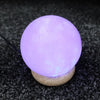 A glowing lavender usb himalayan salt lamp ball with textured surface on a cork base showing hygroscopic properties