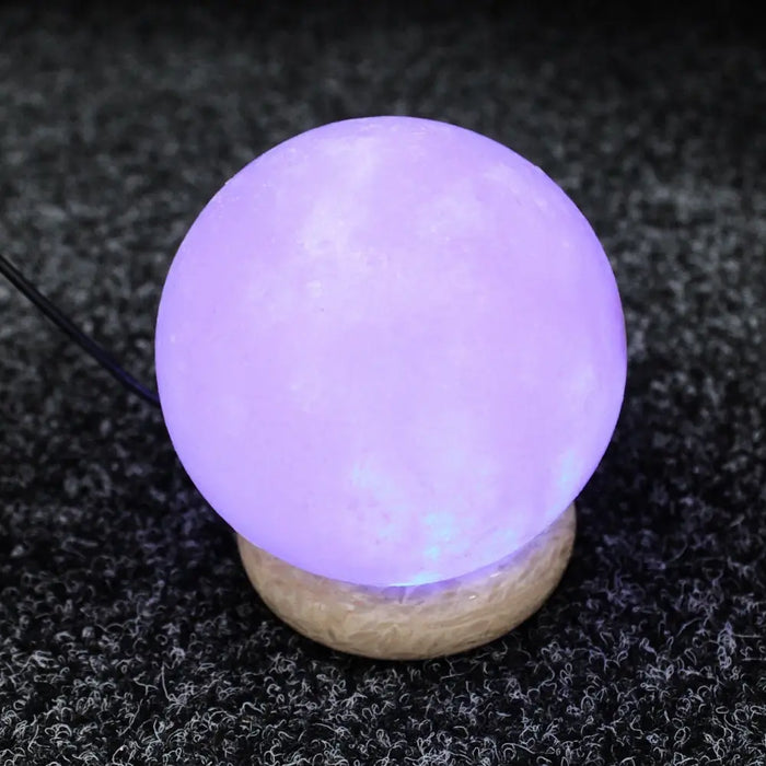 A glowing lavender usb himalayan salt lamp ball with textured surface on a cork base showing hygroscopic properties