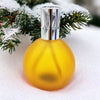 A translucent yellow amber coloured glass colony perfume lamp with a silver cap set on snowy evergreen branches