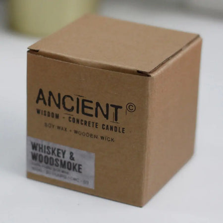 A brown cardboard concrete candle pot with wooden wick labeled whiskey and woodsmoke scent from ancient wisdom