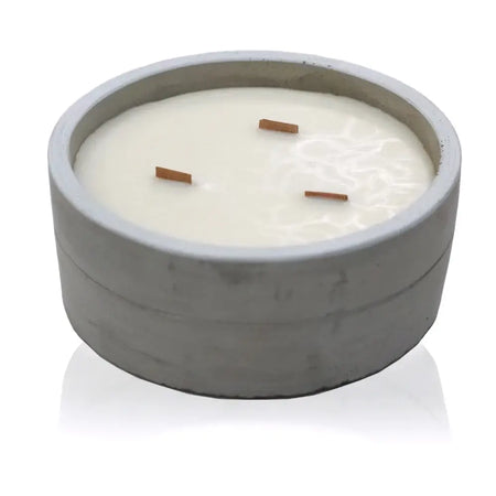 A white concrete candle with three wooden wicks in a textured gray bowl scented with crushed vanilla and orange