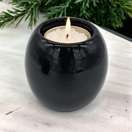 Contemporary black glossy ceramic tealight holder with a lit white tea light inside spherical shape