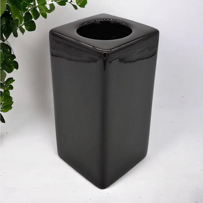 Black glossy ceramic square trash can with circular opening next to a tall contemporary brown ceramic tealight holder