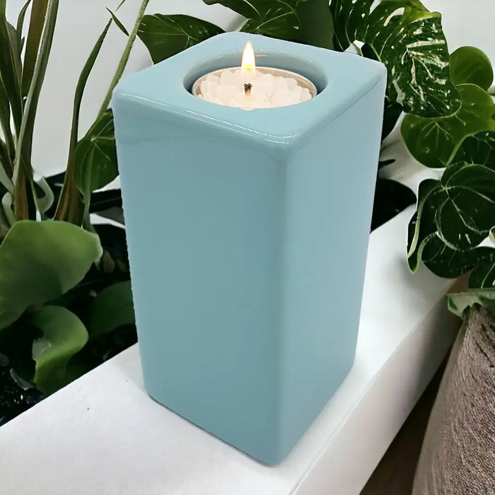A pale blue ceramic tealight holder with a square shape and smooth glossy finish measuring high x 7cm