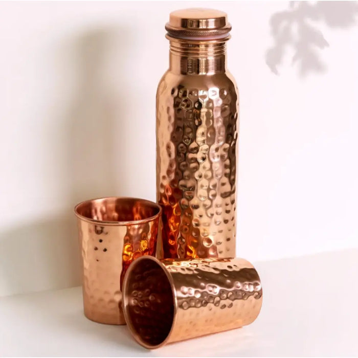 A hammered copper water bottle with matching lid and two cups gift set in warm metallic sheen for warm water use