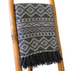 A dark gray and off-white geometric patterned cotton throw blanket with black fringe for cozy home use