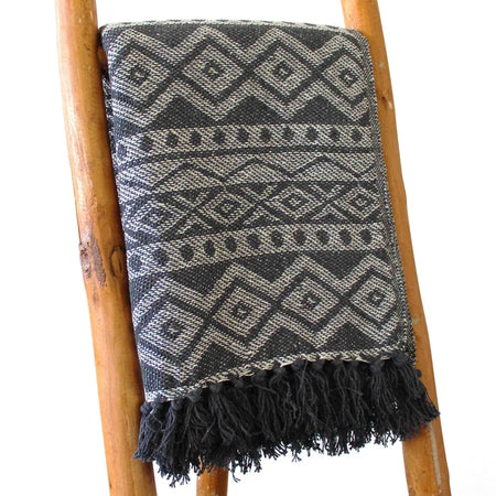 A dark gray and off-white geometric patterned cotton throw blanket with black fringe for cozy home use